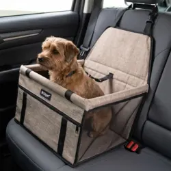 Lille brun hund sidder i et beige autostol til hunde fastgjort på bilens bagsæde.